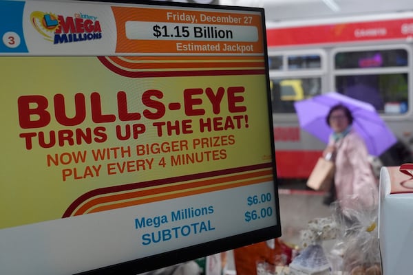 A pedestrian walks behind a sign advertising the estimated $1.15 billion Mega Millions jackpot at Rossi's Deli in San Francisco, Thursday, Dec. 26, 2024. (AP Photo/Jeff Chiu)