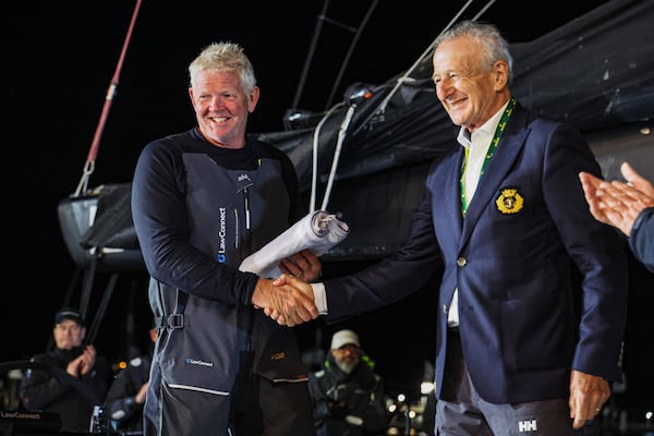 Tony Mutter, left, skipper of Law Connect is presented with the Back Stay flag by Cruising Yacht Club of Australia, Vice Commodore David Jacobs, after winning line honours in the Sydney to Hobart yacht race in Hobart, Australia, Saturday, Dec. 28, 2024. (Salty Dingo via AP)