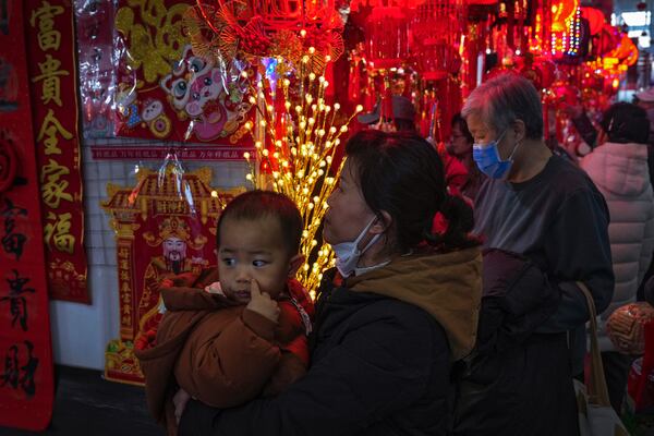 A woman carries a child as she shops at a New Year bazaar set up for the upcoming Chinese Lunar New Year, in Beijing on Jan. 13, 2025. (AP Photo/Andy Wong)