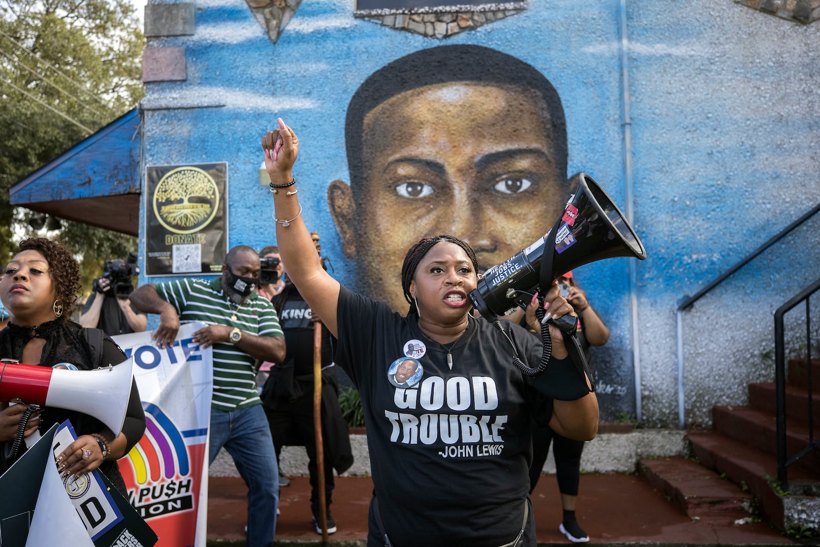 FILE - Civil rights activist Porchse Miller, of Atlanta, shouts into a megaphone in front of a mural of Ahmaud Arbery during march that followed the Wall of Prayer event outside the Glynn County Courthouse, Nov. 18, 2021, in Brunswick, Ga. (AP Photo/Stephen B. Morton, File)