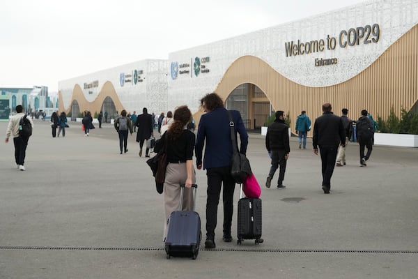 Attendees pull luggage as they walk into the venue for the COP29 U.N. Climate Summit, Saturday, Nov. 23, 2024, in Baku, Azerbaijan. (AP Photo/Sergei Grits)