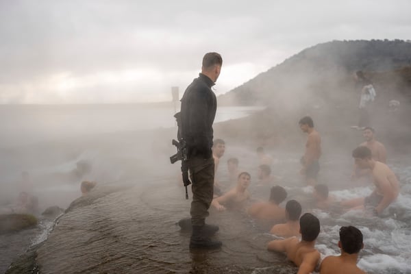 An Israeli soldier stands guard as residents bathe in a hot water coming out of a pipe from a drilling project which exposed a subterranean hydrothermal spring, Mount Bental in the Israeli-controlled Golan Heights, on the day that the ceasefire between Israel and Hizballa began, Wednesday, Nov. 27, 2024. (AP Photo/Ohad Zwigenberg)