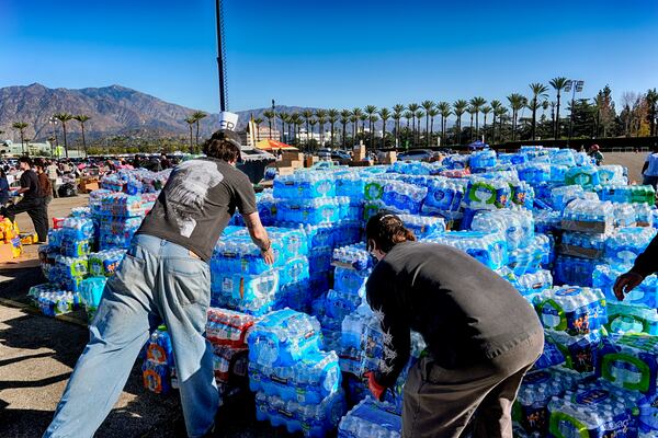 Volunteers stack donated water for people impacted by the Altadena Fire at a donation center at Santa Anita Park in Arcadia, Calif., on Wednesday, Jan. 15, 2025. (AP Photo/Richard Vogel)