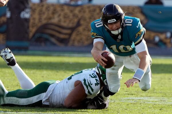 Jacksonville Jaguars quarterback Mac Jones (10) is tripped up by New York Jets defensive end Solomon Thomas (94) during the second half of an NFL football game Sunday, Dec. 15, 2024, in Jacksonville, Fla. (AP Photo/John Raoux)