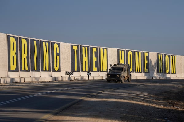 An israeli army vehicle near the Israeli-Gaza border, drives beside a banner reading " Bring them home now" call for the release of hostages held in the Gaza Strip by the Hamas militant group, Wednesday, Jan. 1, 2025. (AP Photo/Ohad Zwigenberg)