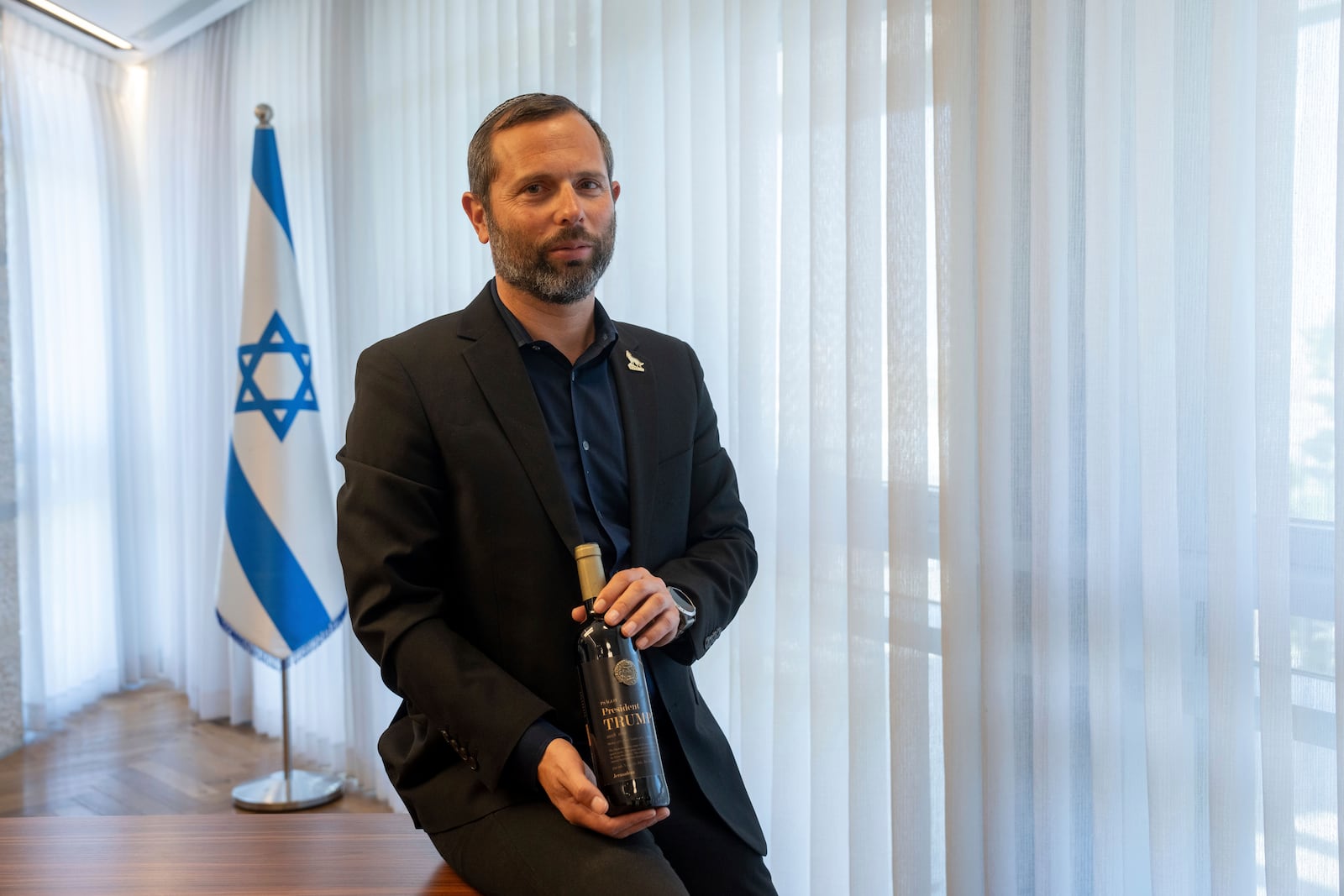 Israel Ganz, chairman of the Yesha settlers council and head of the Mateh Binyamin Regional Council, poses for a portrait holding a bottle of wine bearing the name of U.S. President-elect Donald Trump in the Shaar Binyamin Industrial Park in the West Bank, Monday, Nov. 11, 2024. (AP Photo/Ohad Zwigenberg)