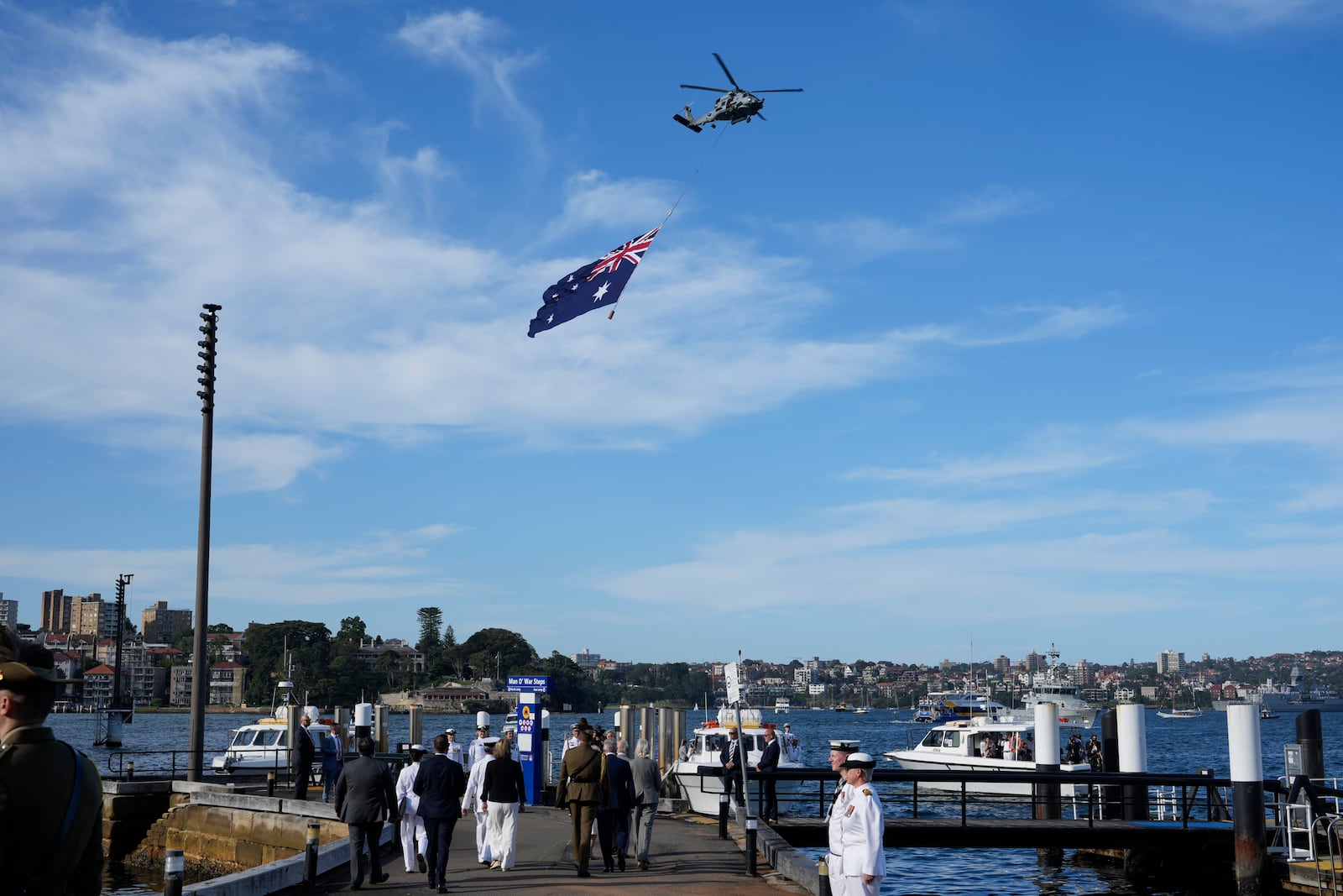 A helicopter flies with a giant Australian flag over the harbor during Britain's King Charles III and Queen Camilla visit at the Sydney Opera House in Sydney, Australia, Tuesday, Oct. 22, 2024. (AP Photo/Mark Baker, Pool)