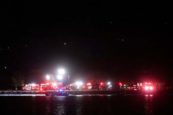 A boat on the Potomac River, cruises past emergency response vehicles seen staging at Joint Base Anacostia Bolling, in the early morning hour, Thursday, Jan. 30, 2025 in Washington, as seen from across the river near Ronald Reagan Washington National Airport in Arlington, Va. (AP Photo/Kevin Wolf)