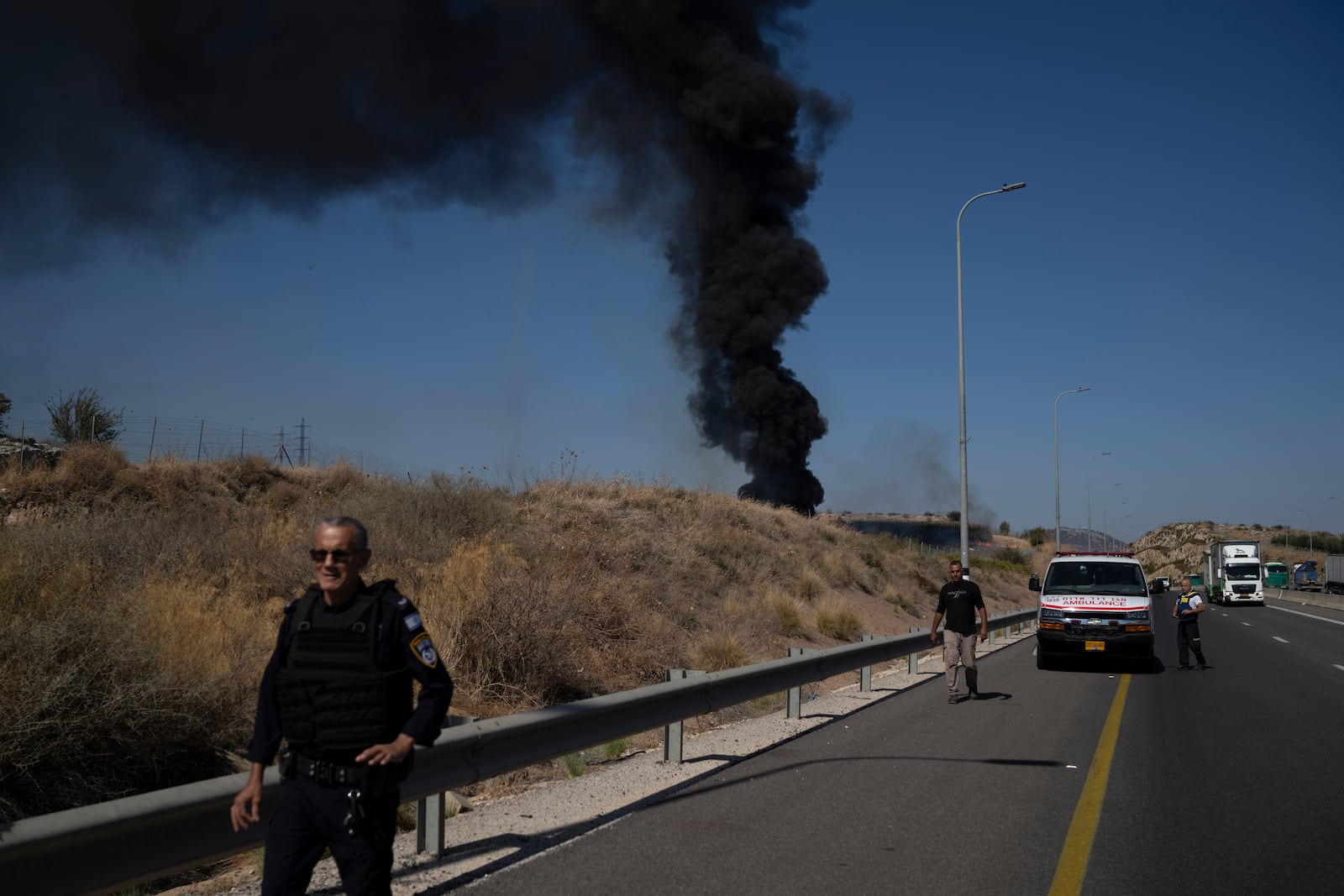 A Israeli police officer walks past site of a fire after a rocket, fired from Lebanon, hit an area near the town of Rosh Pinna, northern Israel, Sunday, Oct. 20, 2024. (AP Photo/Leo Correa)