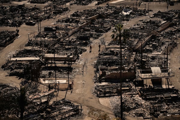 Two people walk along a road in a fire-ravaged community in the aftermath of the Palisades Fire in the Pacific Palisades neighborhood of Los Angeles, Monday, Jan. 13, 2025. (AP Photo/John Locher)