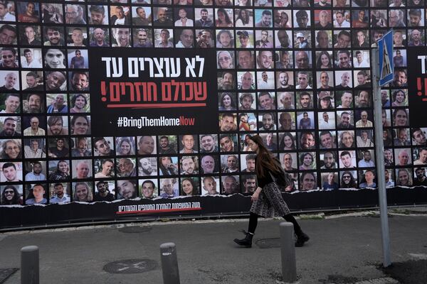 A woman walks past photos of hostages held by Hamas in the Gaza Strip, in Jerusalem, Friday, Jan. 17, 2025. (AP Photo/Mahmoud Illean)