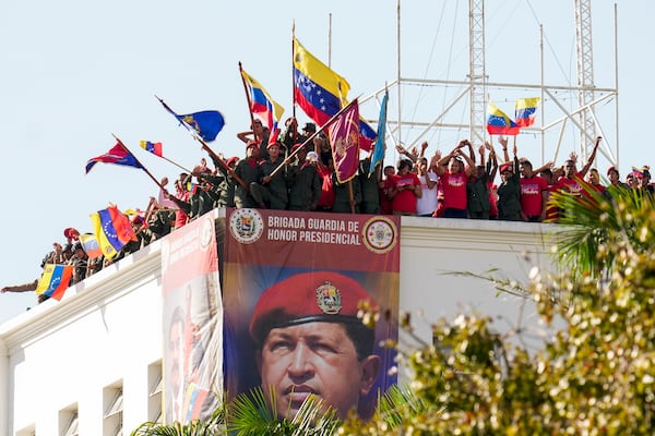 Military and government supporters wave from the roof of the presidential guard headquarters as Venezuelan President Nicolas Maduro speaks at the presidential palace in Caracas, Venezuela, Friday, Jan. 10, 2025, on his inauguration day for a third term. The banner shows Maduro's predecessor, the late President Hugo Chavez. (AP Photo/Matias Delacroix)