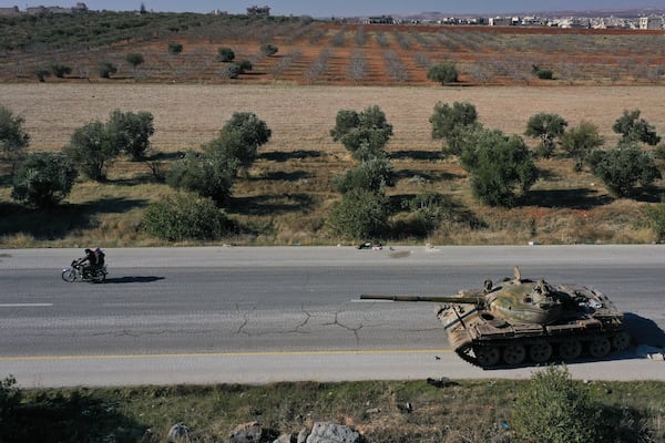 Syrian opposition fighters ride on a motorcycle by an abandoned Syrian army armoured vehicle on a road in the outskirts of in Khan Sheikhoun, southwest of Aleppo, Sunday, Dec. 1, 2024. Syrian opposition insurgency launched a campaign on Wednesday with a two-pronged attack on Aleppo and the countryside around Idlib.(AP Photo/Ghaith Alsayed)