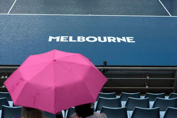 Spectators wait under umbrellas as rain suspends play during first round matches at the Australian Open tennis championship in Melbourne, Australia, Sunday, Jan. 12, 2025. (AP Photo/Manish Swarup)