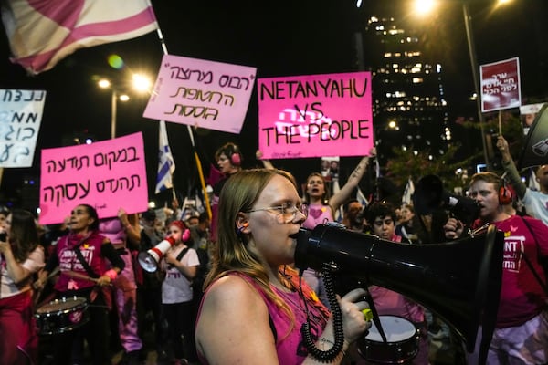 People shout slogans during a protest against Prime Minister Benjamin Netanyahu's government and call for the release of hostages held in the Gaza Strip by the Hamas militant group, in Tel Aviv, Israel, Saturday, Nov. 23, 2024. Boards on the left read in Hebrew: "The boss is satisfied, the hostages are dying" and "Instead of consciousness, make a deal". (AP Photo/Maya Alleruzzo)