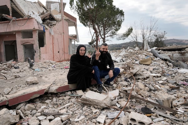 Lebanese citizens flash victory signs, as they sit on the rubble of a destroyed house caused by the Israeli air and ground offensive, in Aita al-Shaab, a Lebanese border village with Israel, south Lebanon, Sunday, Jan. 26, 2025. (AP Photo/Bilal Hussein)