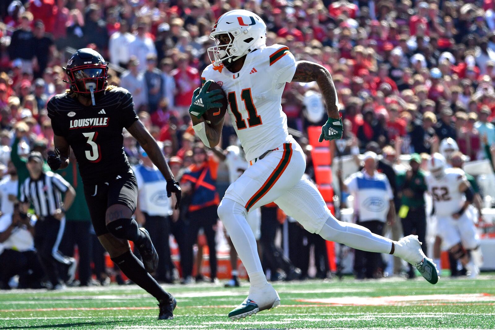 Miami wide receiver Samuel Brown (11) during the first half of an NCAA college football runs from the pursuit of Louisville defensive back Quincy Riley (3) to score game in Louisville, Ky., Saturday, Oct. 19, 2024. (AP Photo/Timothy D. Easley)