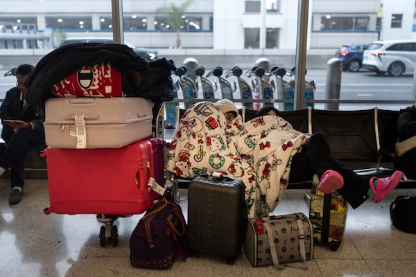 Two travelers nap near the Alaska Airlines ticketing area at the Los Angeles International Airport in Los Angeles, Tuesday, Dec. 24, 2024. (AP Photo/Jae C. Hong)