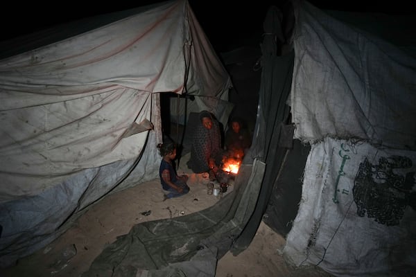 Shireen Daifallah, who was displaced with her children from northern Gaza, checks the fire next to their tent at a camp for displaced people in Deir al-Balah. Gaza Strip, Saturday, Nov. 30, 2024. (AP Photo/Abdel Kareem Hana)