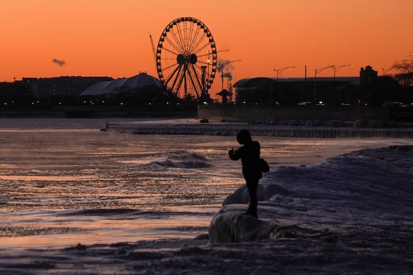 A person stands on ice at Oak Street Beach along the shore of Lake Michigan to take pictures before the sunrise Monday, Jan. 20, 2025, in Chicago, as the weather service issued cold weather advisories across the Great Lakes region as high temperatures in many places were expected only to rise into the single digits Monday and Tuesday. (AP Photo/Kiichiro Sato)