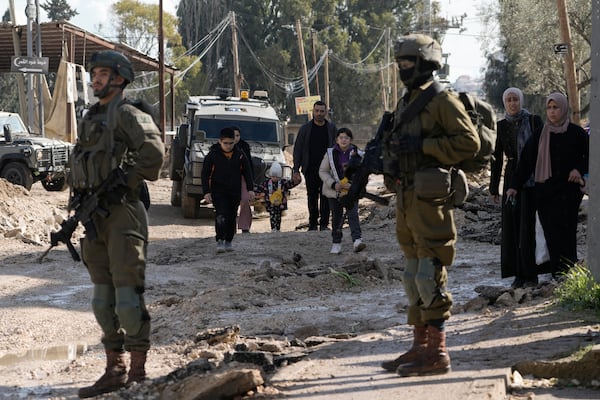 Israeli soldiers stand guard as Palestinians displaced by an Israeli military operation evacuate from the Jenin refugee camp in the West Bank carry their belongings, Thursday, Jan. 23, 2025. (AP Photo/Majdi Mohammed)