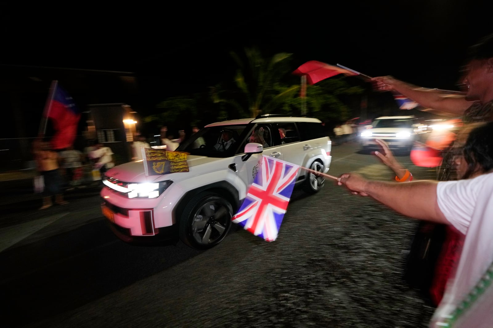 People wave flags as Britain's King Charles III and Queen Camilla arrive in the village of Siumu, Samoa, on Wednesday, Oct. 23, 2024. (AP Photo/Rick Rycroft)