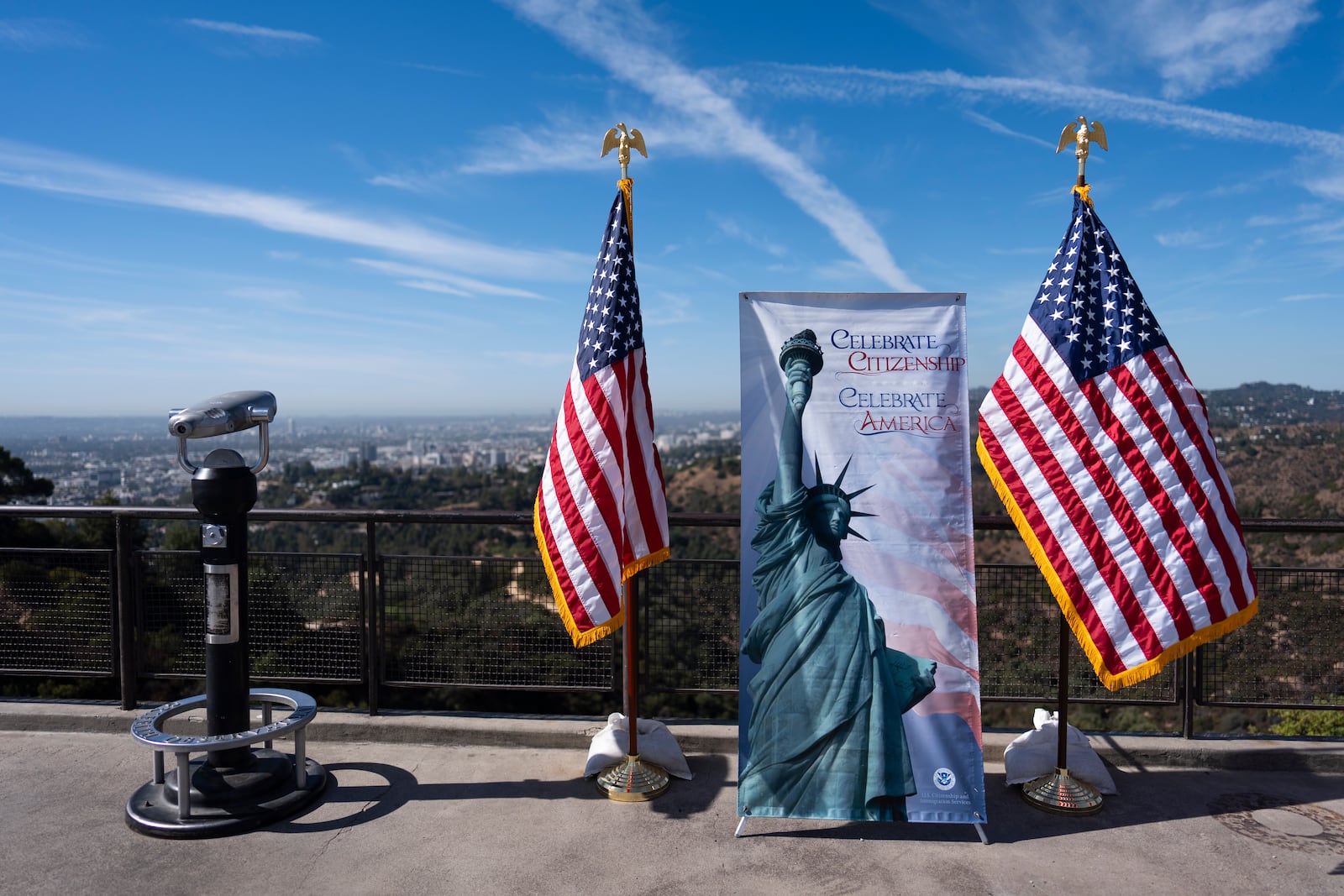 Two American flags and a banner featuring the Statue of Liberty stand as part of a naturalization ceremony at Griffith Observatory in Los Angeles, Monday, Oct. 21, 2024. (AP Photo/Jae C. Hong)