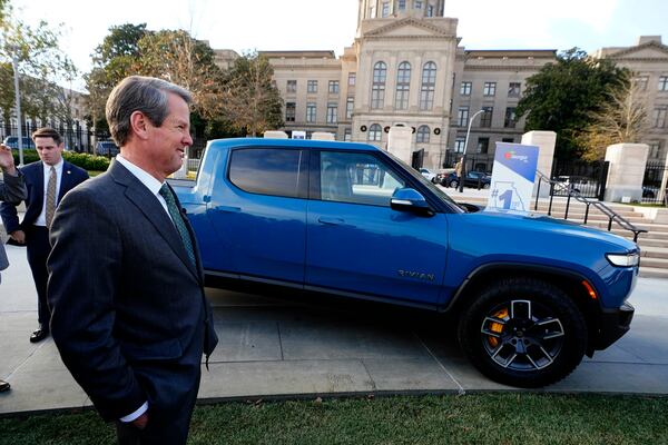 FILE - Gov. Brian Kemp smiles as he stands next to a Rivian electric truck during a ceremony to announce that the electric truck maker plans to build a $5 billion battery and assembly plant east of Atlanta projected to employ 7,500 workers, Dec. 16, 2021, in Atlanta. (AP Photo/John Bazemore, File)