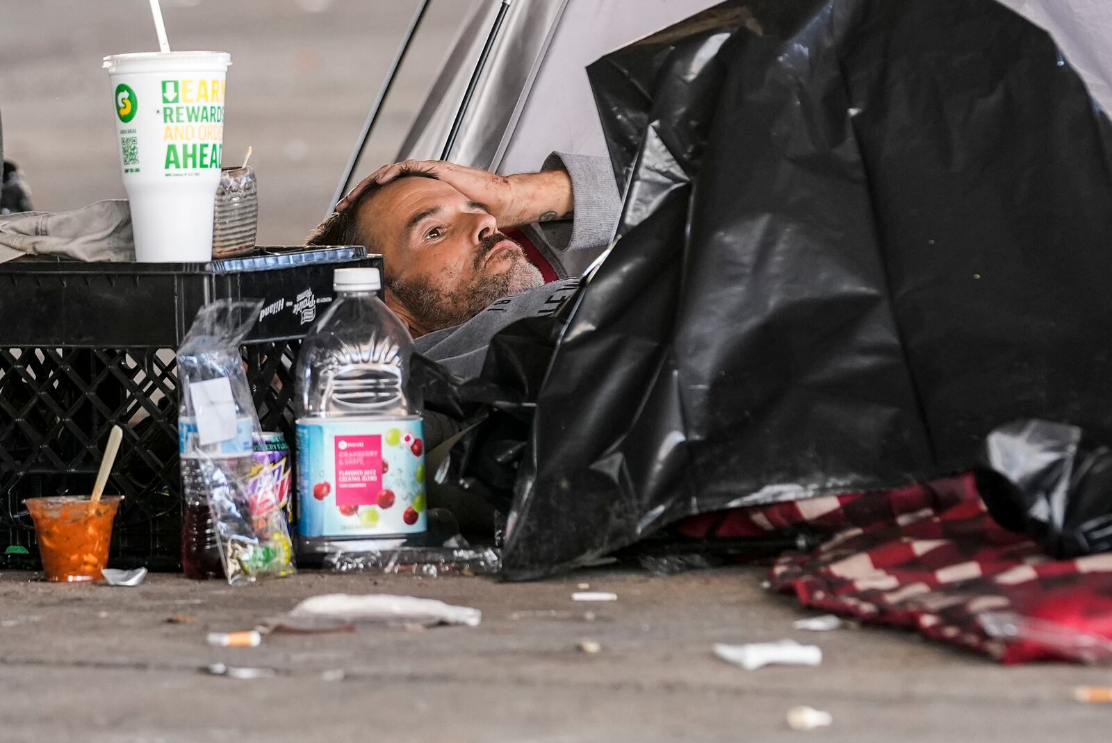 A man in a homeless encampment lays among possessions after Louisiana State police gave instructions for them to move to a different pre-designated location as they perform a sweep in advance of a Taylor Swift concert in New Orleans, Wednesday, Oct. 23, 2024. (AP Photo/Gerald Herbert)