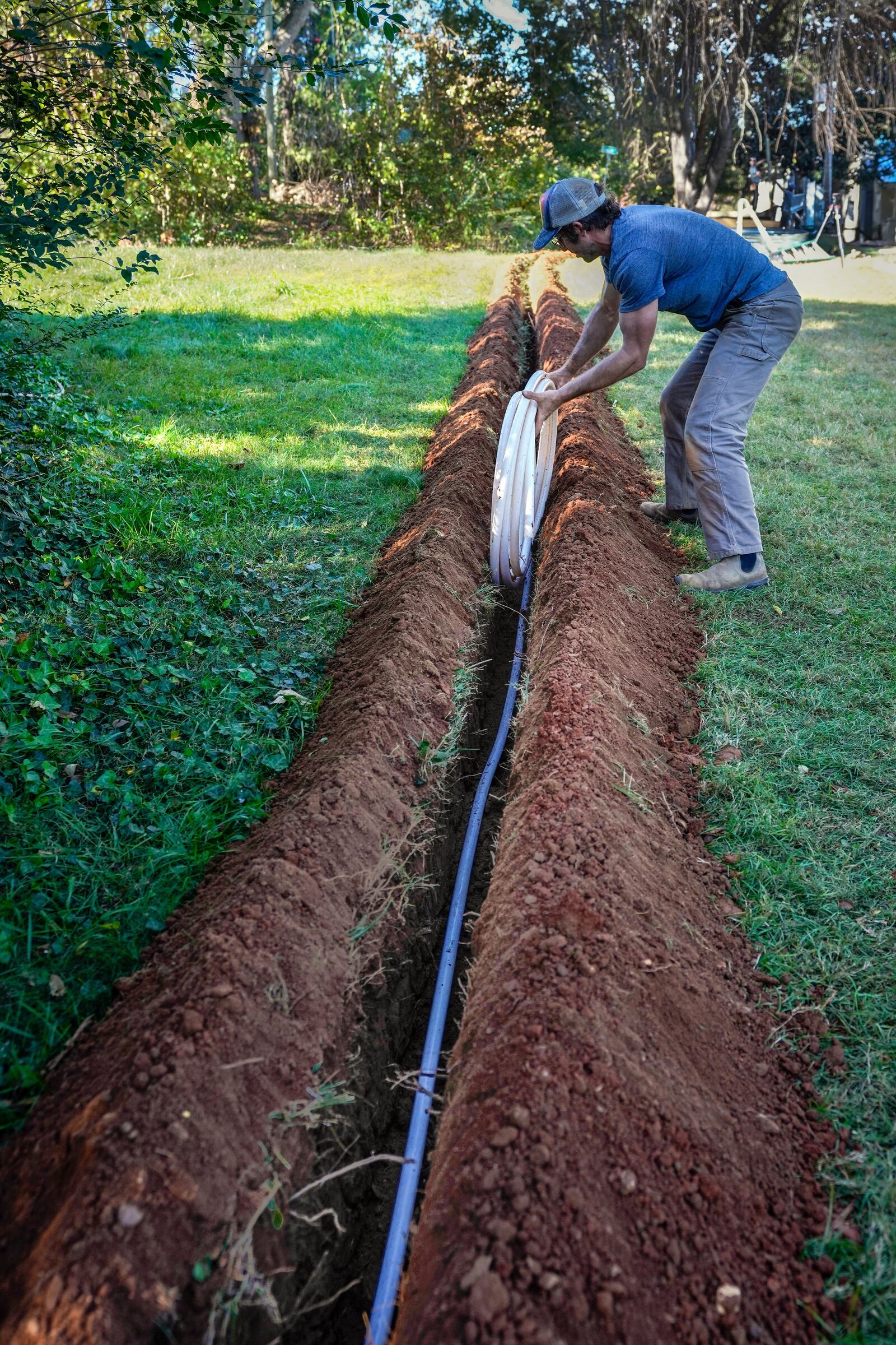 Jeffrey Martyn, a plumber and electrician puts pipe into a freshly made ditch on an urban farm that belongs to Bountiful Cities, a nonprofit organization, Monday, Oct. 14, 2024, in Asheville, N.C. (AP Photo/Kathy Kmonicek)