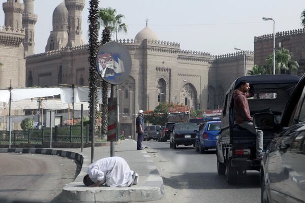 FILE - The motorcade of former U.S. President Jimmy Carter passes a man praying in the street beneath an election poster for presidential candidate Khaled Ali during the election of a new president after the fall of ex-President Hosni Mubarak in Cairo, May 23, 2012. (AP Photo/Thomas Hartwell, File)