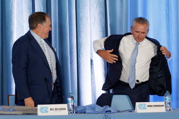 New North Carolina football coach Bill Belichick, left, looks on as UNC athletic director Bubba Cunningham, right, puts on a sport coat with cut-off sleeves during an NCAA college football press conference, Thursday, Dec. 12, 2024, in Chapel Hill, N.C. (AP Photo/Ben McKeown)