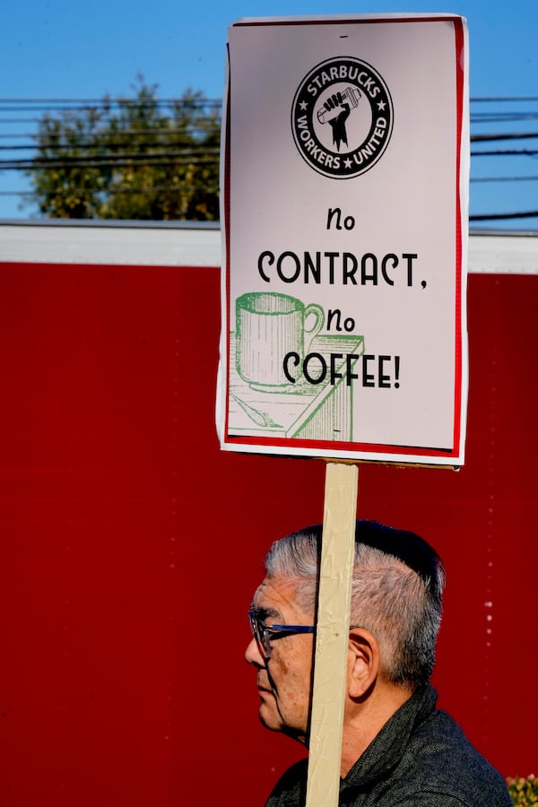 A protester carries a sign joining with Starbucks workers during the start of a five-day strike to protest a lack of progress in contract negotiations with the company Friday, Dec. 20, 2024, in Burbank, Calif. (AP Photo/Damian Dovarganes)