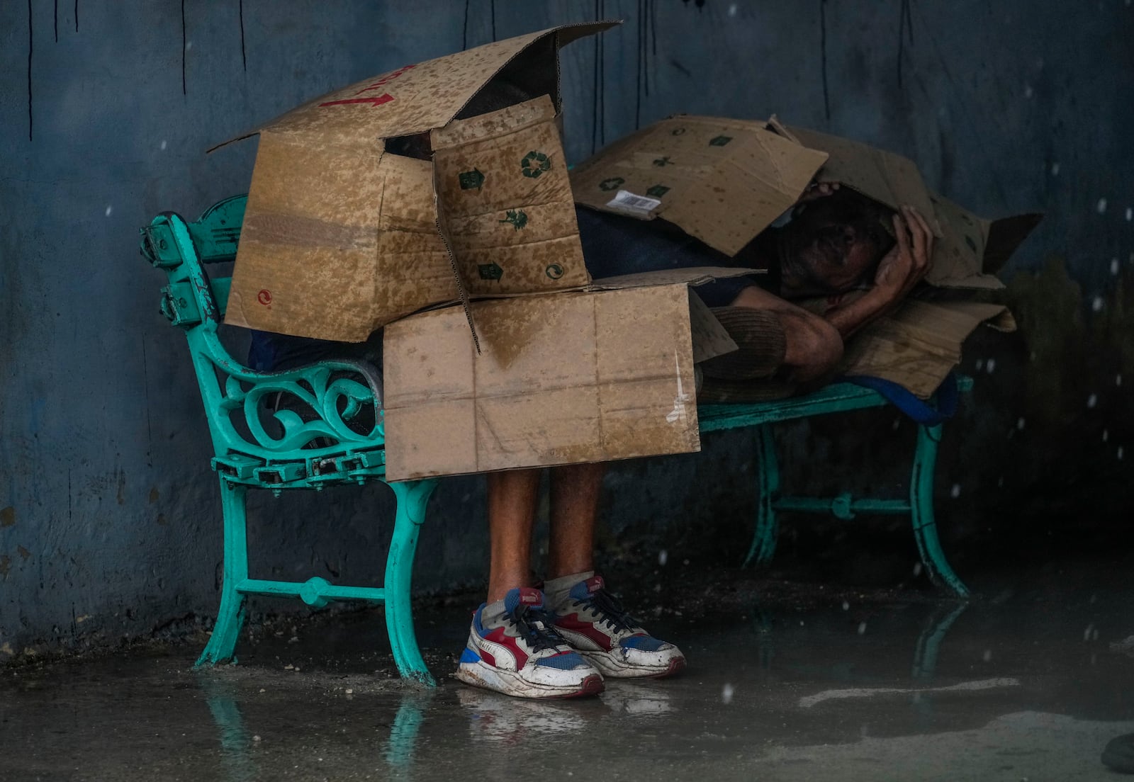 People shelter under cardboard from the winds and rain from Hurricane Rafael at a bus stop in Havana, Cuba, Wednesday, Nov. 6, 2024. (AP Photo/Ramon Espinosa)