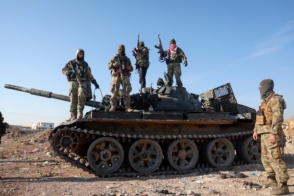 Syrian opposition fighters stand atop a seized military armored vehicle on the outskirts of Hama, Syria, Tuesday, Dec. 3, 2024. (AP Photo/Ghaith Alsayed)