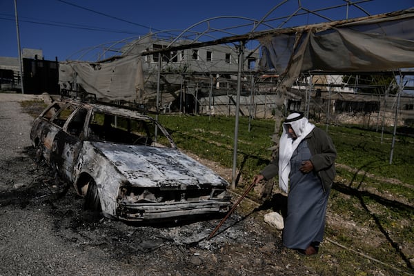 A Palestinian stands beside a torched car in the aftermath of an attack by Israeli settlers in the West Bank village of Jinsafut, Tuesday, Jan. 21, 2025. (AP Photo/Majdi Mohammed)