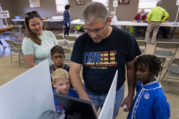 Mike Young, joined by his wife Erin Young, left, and their three adopted kids, Gianna, 7, right, Isaac, 5, third from right, and Lucas, 8, second from left, votes for Donald Trump on Election Day, Tuesday, Nov. 5, 2024, at the Trenton Township building in Sunbury, Ohio. (AP Photo/Carolyn Kaster)