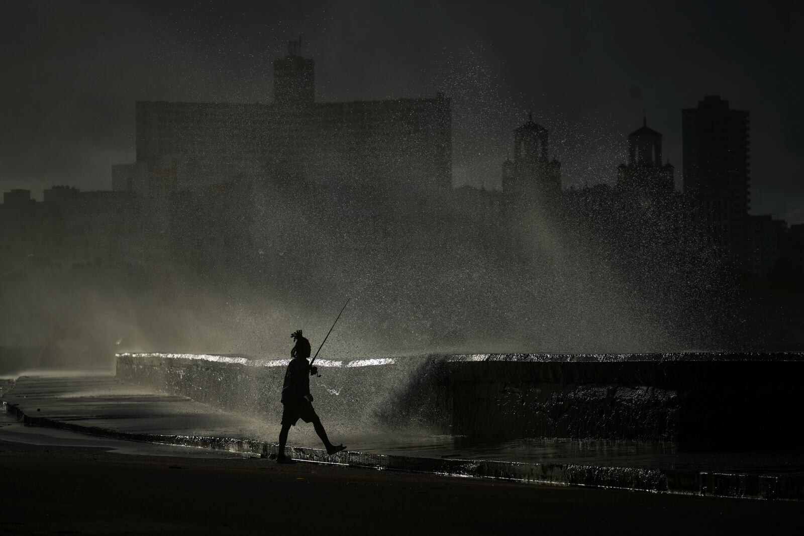 A person fishes along the boardwalk as waves break in Havana, Monday, Oct. 21, 2024. (AP Photo/Ramon Espinosa)