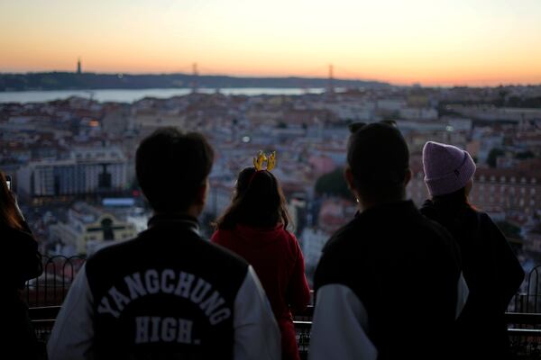 A woman wearing reindeer antlers watches the sun set from the Our Lady of the Hill viewpoint overlooking Lisbon, Tuesday, Dec. 24, 2024. (AP Photo/Armando Franca)