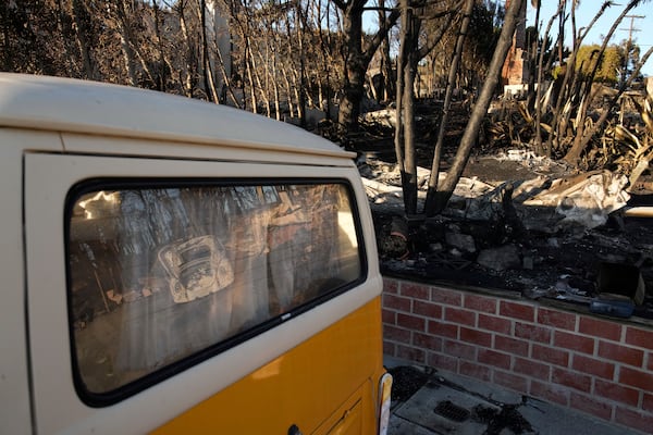 A destroyed Volkswagen Beetle is reflected in the back window of an intact Volkswagen vehicle in the aftermath of the Palisades Fire in the Pacific Palisades neighborhood of Los Angeles, Monday, Jan. 13, 2025. (AP Photo/John Locher)