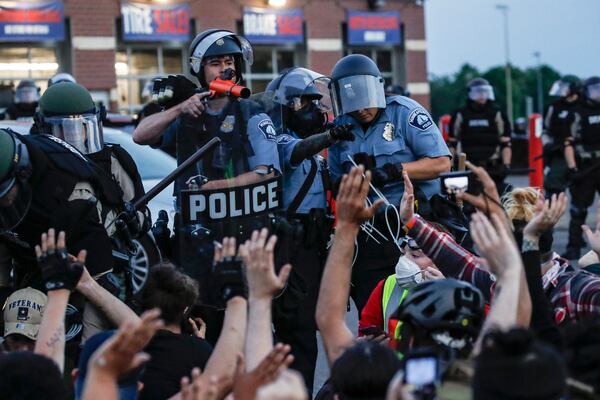 FILE - A police officer points a hand cannon at protesters who have been detained pending arrest on South Washington Street in Minneapolis, May 31, 2020, as protests continued following the death of George Floyd. (AP Photo/John Minchillo, File)